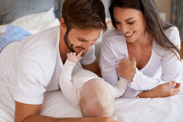 Couple laying on bed with their baby | Safe Sleep Space