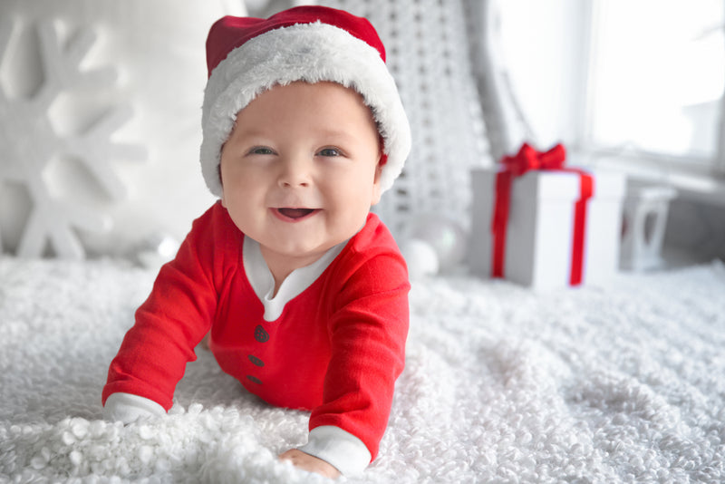 Smiling baby in Christmas hat & red outfit on white rug | Safe Sleep Space