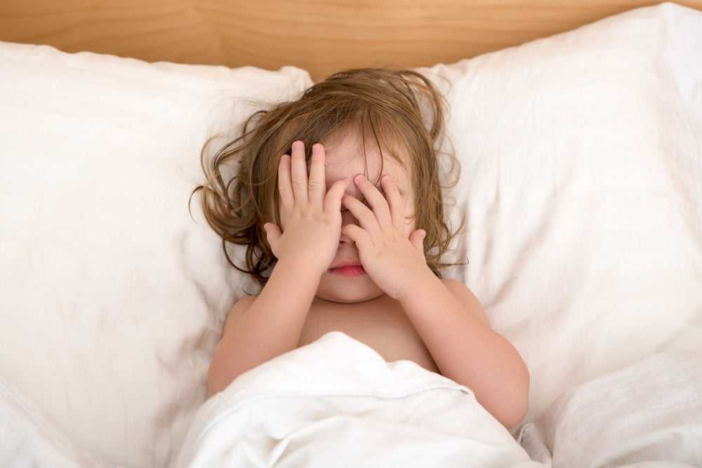 Toddler laying in bed covering face with hands | Safe Sleep Space